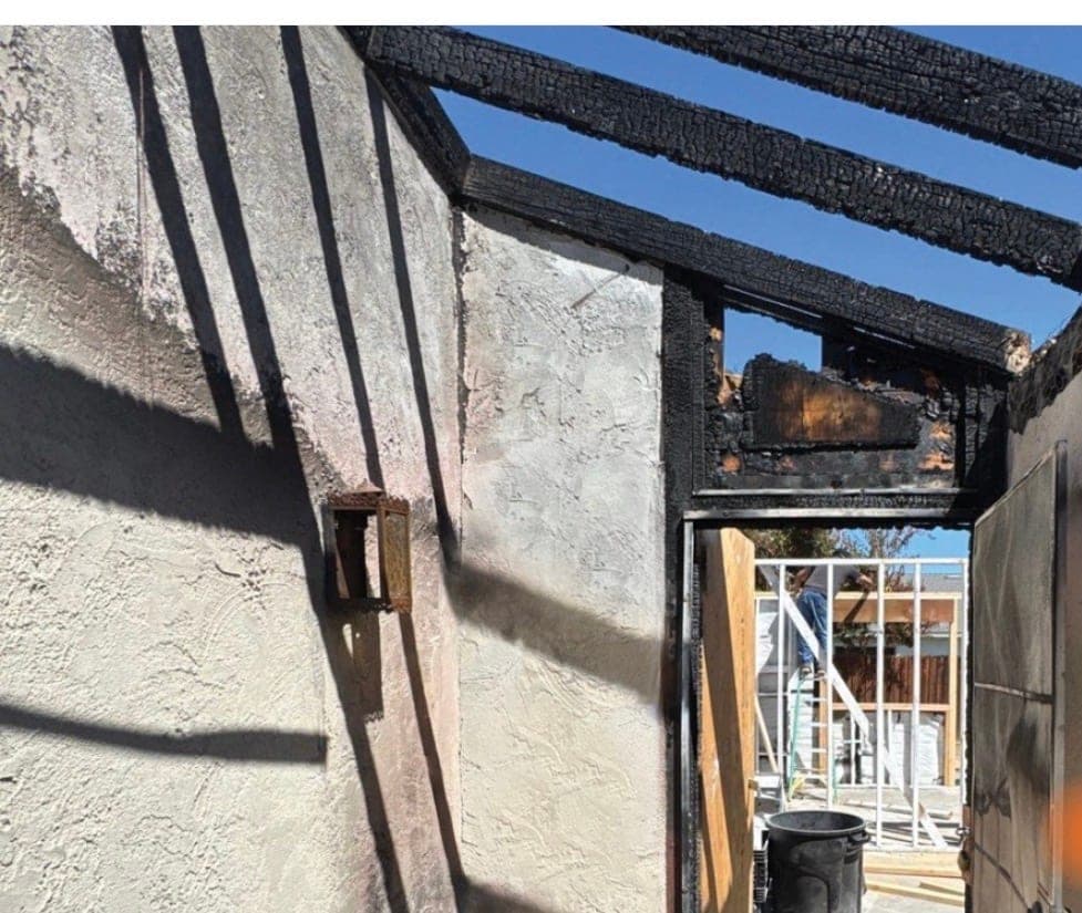 Charred beams and smoke-stained stucco at the entry of a fire-damaged house awaiting emergency stabilization